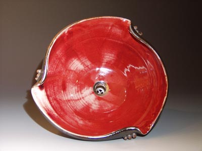 Voderansicht eines symetrisch gebogenen, individuell handangerfertigten Waschbeckens mit roter Glasur an der Innenseite und Ölfleckglasur an der Außenseite.